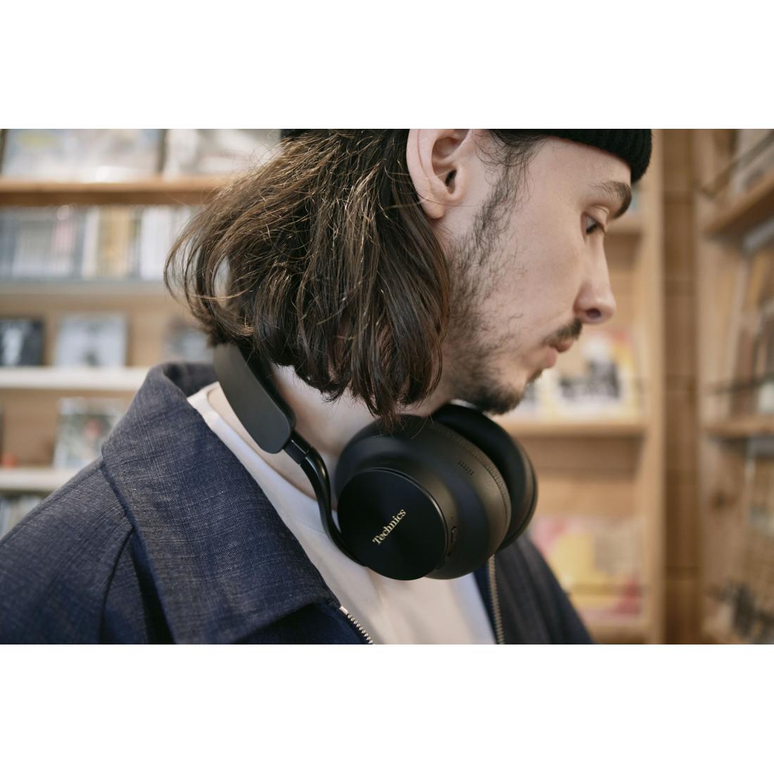 A man wearing black over-ear headphones around his neck, shown in profile against a blurred bookstore background.