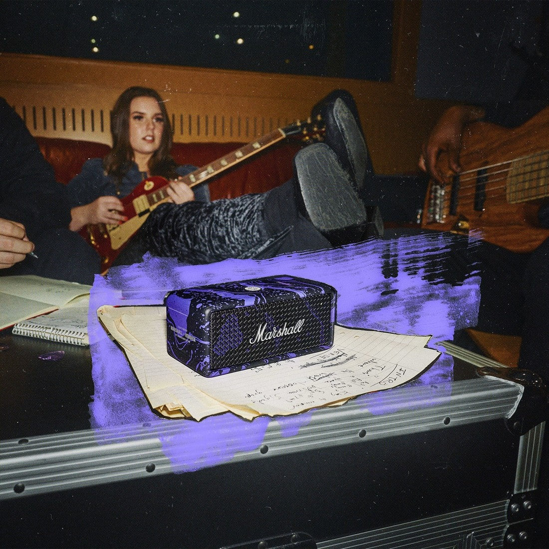 A woman with a guitar sits on a couch, Emberton III Hendrix Edition, papers, and notes are in the foreground.