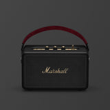 Marshall Kilburn III Black and Brass portable Bluetooth speaker, featuring a gold logo and brown carrying handle, is shown from the front against a plain background.