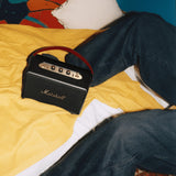 Marshall Kilburn III Black and Brass portable speaker sits on a yellow bedspread next to a person in dark jeans.