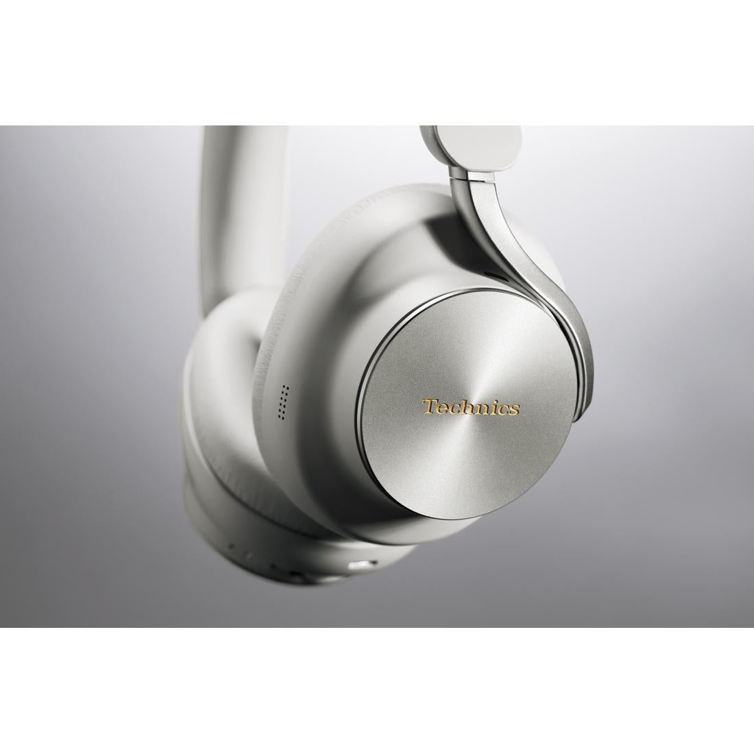 A close-up studio shot of a Technics over-ear wireless headphone in metallic silver, showing the outer ear cup with the gold Technics logo and the headband attachment.