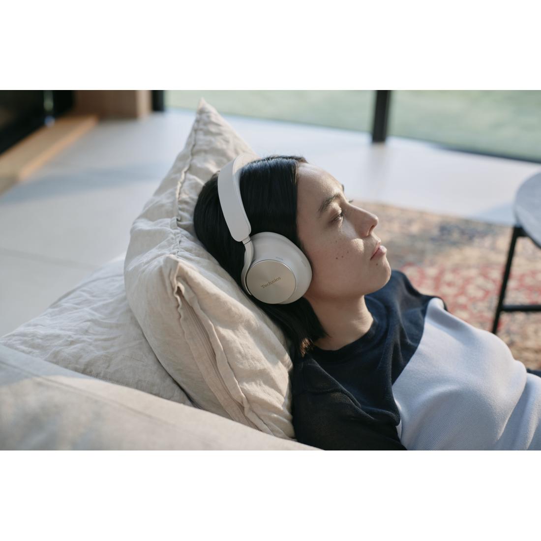 A woman reclining on a couch wearing white over-ear headphones in a softly lit indoor setting.