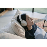 A woman reclining on a couch wearing white over-ear headphones in a softly lit indoor setting.