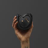 A folded pair of Marshall Monitor III A.N.C. Black bluetooth over-ear headphones in a hand against a dark gray background.