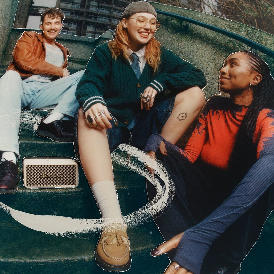 Three people sit on outdoor steps, while music plays from the Marshall Middleton II Cream portable Bluetooth speaker nearby.
