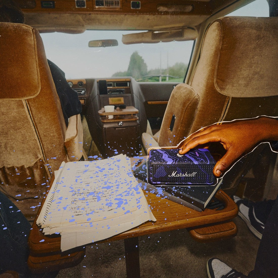 Emberton III Hendrix Edition speaker on a fold-out table in a car, next to a notebook.